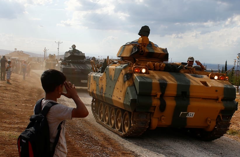 A boy salutes as Turkish Armed Forces vehicles drive pass by a village on the Turkish-Syrian border line in Reyhanli, Hatay province, Turkey October 11, 2017.  (photo credit: REUTERS/OSMAN ORSAL)