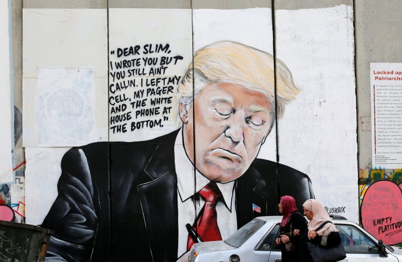 Palestinian women walk by a mural of Donald Trump on the West Bank separation wall, October 2017 (photo credit: AMMAR AWAD / REUTERS)