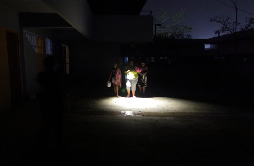People who have lost their homes after Hurricane Maria hit the island in September, walk with the help of a flashlight at a school turned shelter, in Toa Baja, Puerto Rico October 18, 2017. (photo credit: REUTERS)