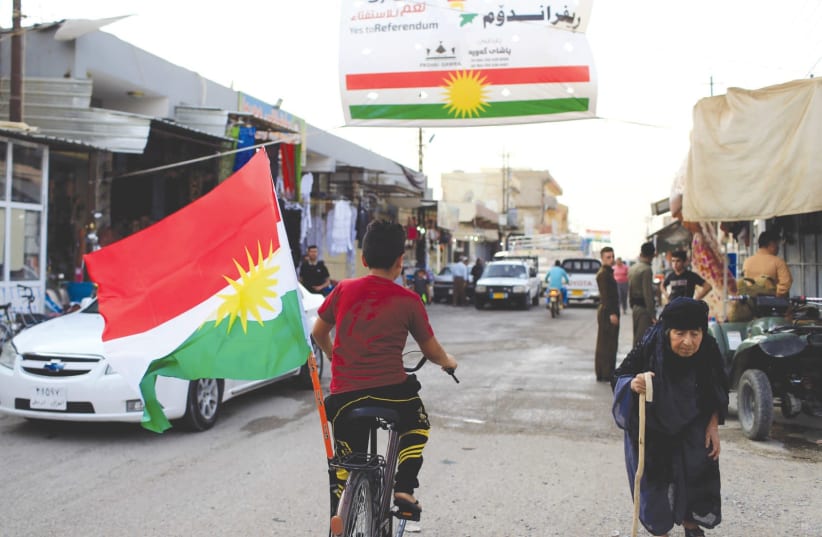 A BOY rides a bicycle with the flag of Kurdistan in Tuz Khurmato, Iraq. (photo credit: REUTERS)