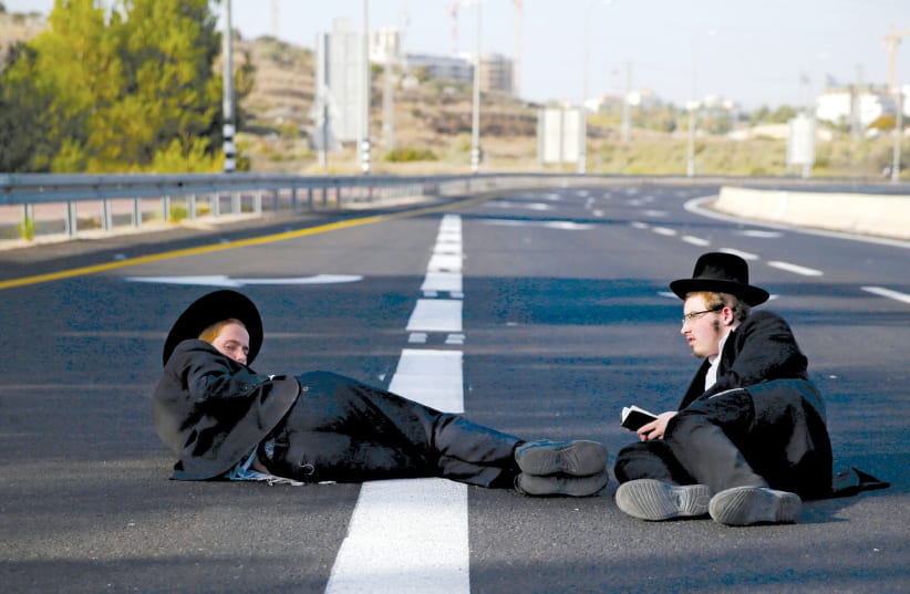 ULTRA-ORTHODOX men sit on a road during the ‘day of rage’ protest near Modi’in on October 19 (photo credit: AMMAR AWAD/REUTERS)