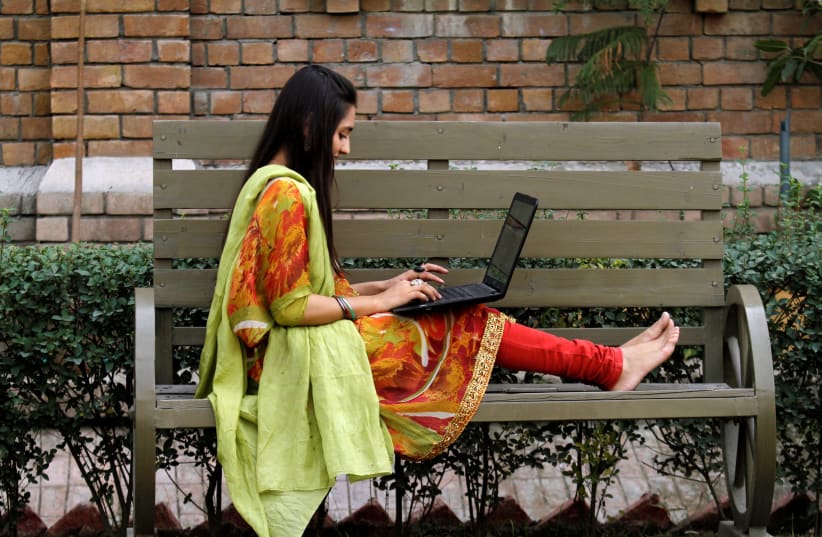 A student works on her computer sitting on a bench at Shaheed Benazir Bhutto Women's University in Peshawar, Pakistan  (photo credit: REUTERS/ FAYAZ AZIZ)