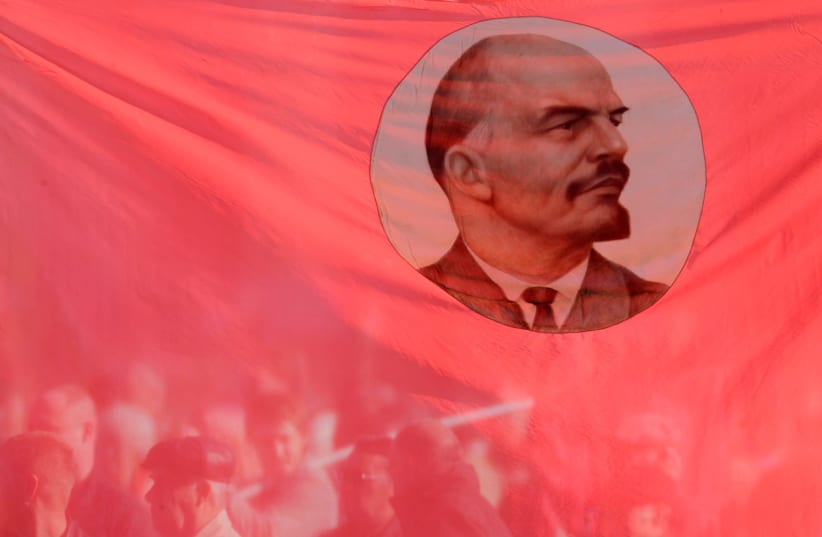 Russians hold up a flag emblazoned with Communist leader Vladimir Lenin (photo credit: EDUARD KORNIYENKO)