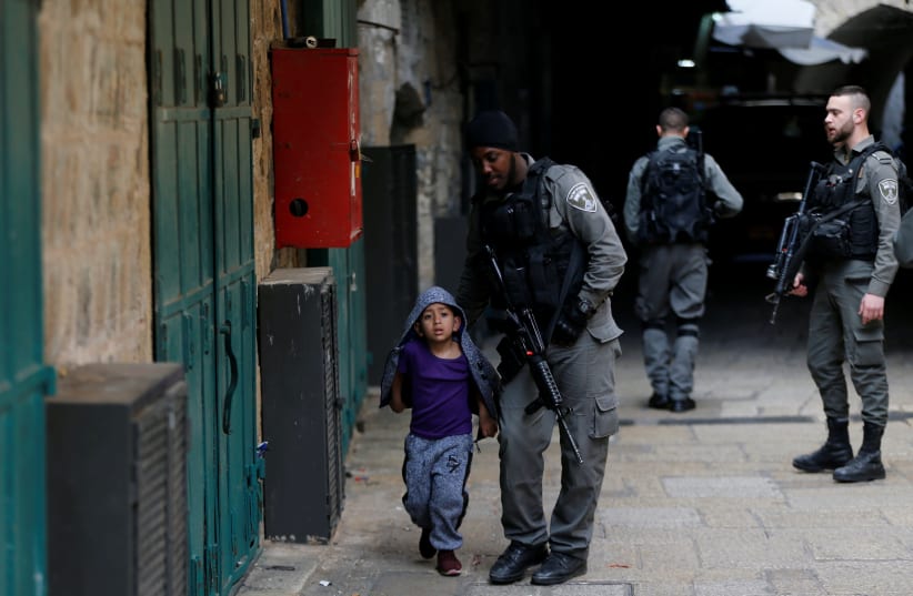 An Israeli border policeman escorts a boy away from a blocked alley in Jerusalem (photo credit: AMMAR AWAD / REUTERS)