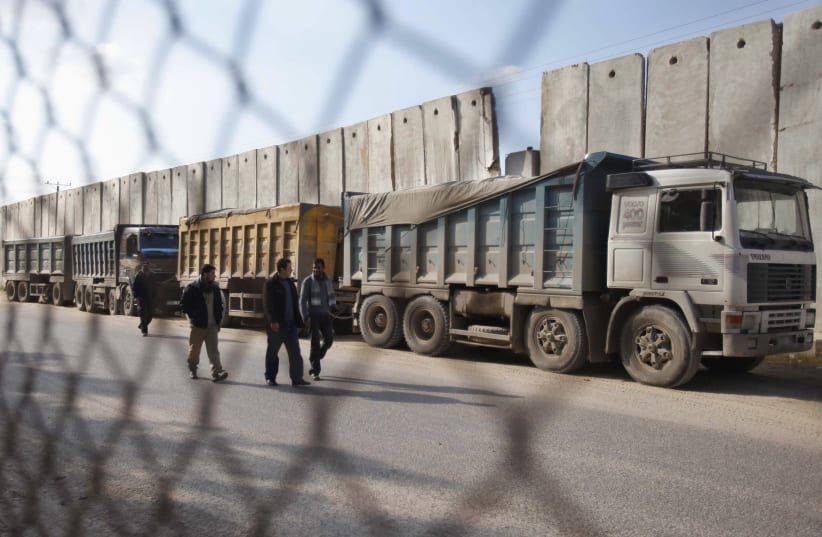 Palestinians walk past trucks loaded with gravel at the Kerem Shalom crossing between Israel and the southern Gaza Strip December 30, 2012. (photo credit: REUTERS)