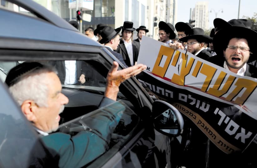A DRIVER argues with haredi men as they protest against the detention of members of their community who failed to report to a military recruiting office, in Jerusalem last month. The placard in Hebrew reads, ‘Fans of those imprisoned from the Torah world.’ ( (photo credit: AMMAR AWAD / REUTERS)