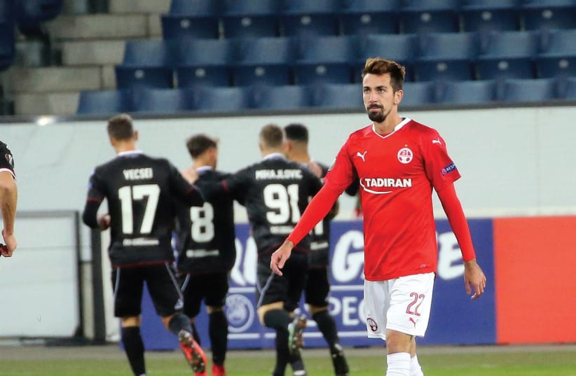 Hapoel Beersheba midfielder Isaac Cuenca walks away disappointed while Lugano players celebrate scoring their winner in the background in a 1-0 victory in Europa League action in Switzerland. (photo credit: UDI ZITIAT)