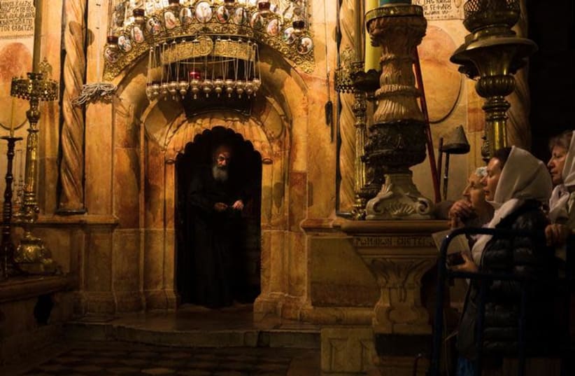Worshippers stand nearby as a priest peers out from the Edicule, the burial place housing the purported tomb of Jesus, at the Church of the Holy Sepulchre in Jerusalem's Old City November 3, 2017 (photo credit: REUTERS/Ronen Zvulun)