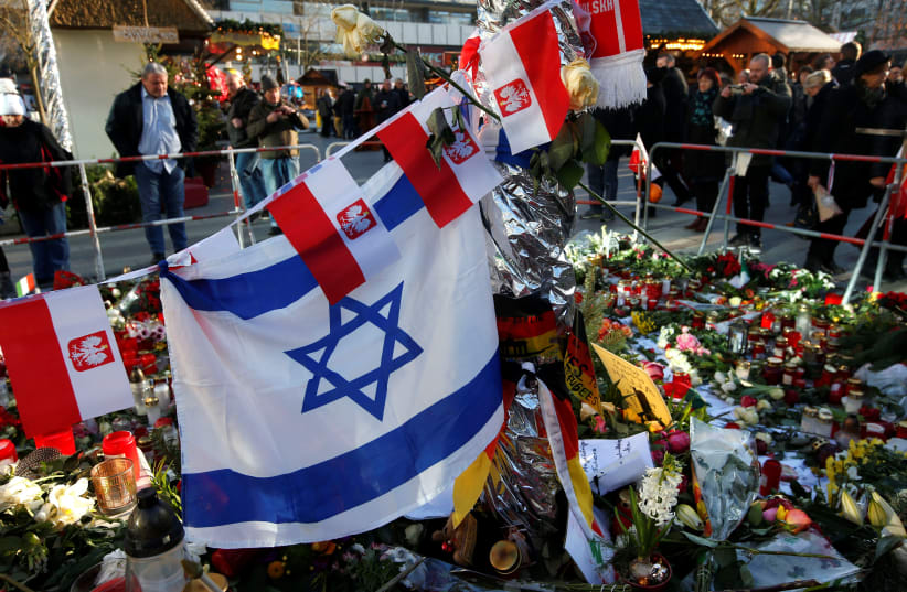 Israeli and Polish national flags are pictured together with flowers and candles placed at the Christmas market at Breitscheid square in Berlin, Germany. (photo credit: REUTERS/FABRIZIO BENSCH)