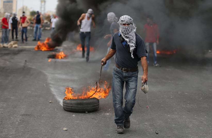 A Palestinian protester drags a burning tyre during clashes with Israeli troops near the Jewish settlement of Bet El, near the West Bank city of Ramallah October 23, 2015. (photo credit: MOHAMAD TOROKMAN/REUTERS)