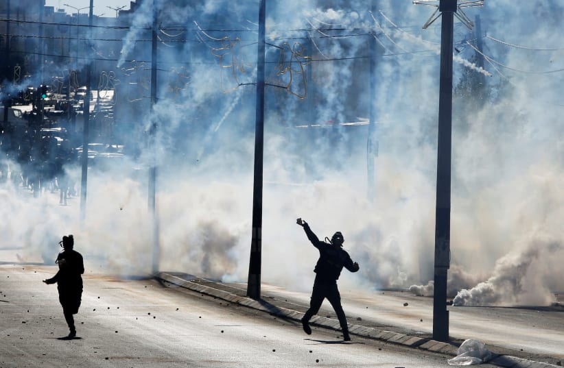 A Palestinian protester hurls stones as tear gas is fired by Israeli troops during clashes as Palestinians call for a "day of rage" in response to US President Donald Trump's recognition of Jerusalem as Israel's capital, in the West Bank city of Bethlehem December 8, 2017  (photo credit: MUSSA QAWASMA / REUTERS)