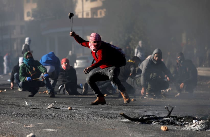 A Palestinian protester hurls stones towards Israeli troops during clashes as Palestinians respond to US President Donald Trump's recognition of Jerusalem as Israel's capital, near the Jewish settlement of Beit El, near the West Bank city of Ramallah (photo credit: MOHAMAD TOROKMAN/REUTERS)