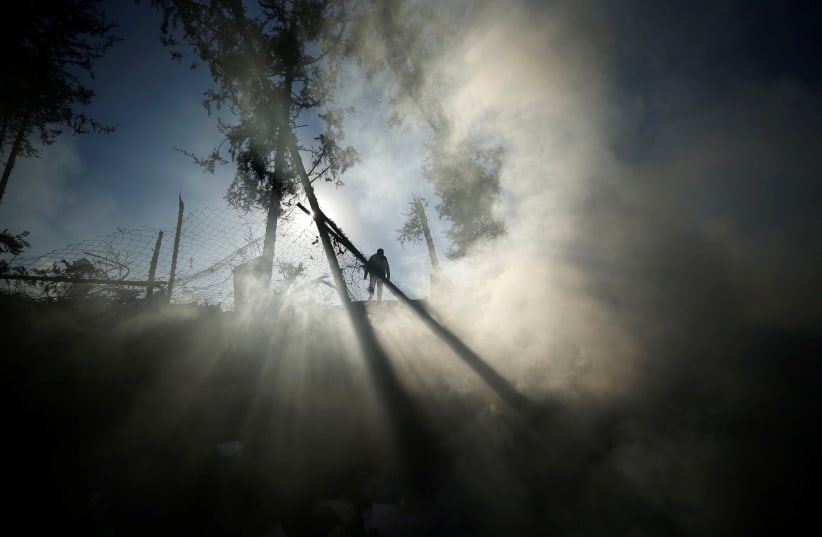 Smoke is seen as a Palestinian man inspects a militant target that was hit in an Israeli airstrike in the northern Gaza Strip December 9, 2017.  (photo credit: MOHAMMED SALEM/ REUTERS)