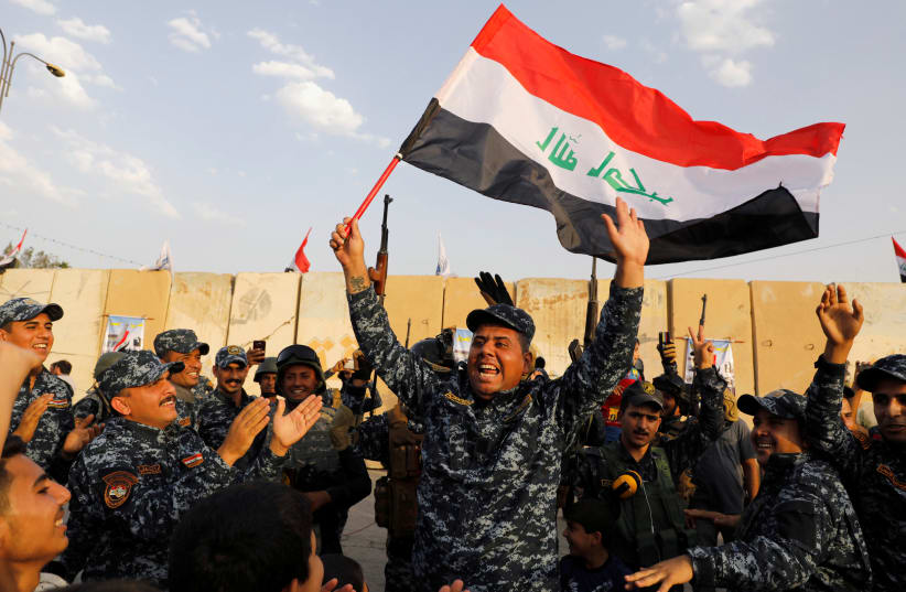 A member of Iraqi Federal Police waves an Iraqi flag as they celebrate victory of military operations against the Islamic State militants in West Mosul, Iraq July 2, 2017 (photo credit: REUTERS)