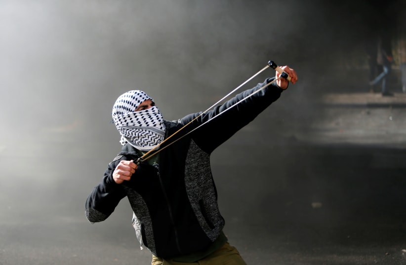 A Palestinian protester uses a sling shot to hurl stones towards Israeli troops during clashes as Palestinians call for a "day of rage" in response to US President Donald Trump's recognition of Jerusalem as Israel's capital, in the West Bank city of Bethlehem December 8, 2017. (photo credit: MUSSA QAWASMA / REUTERS)