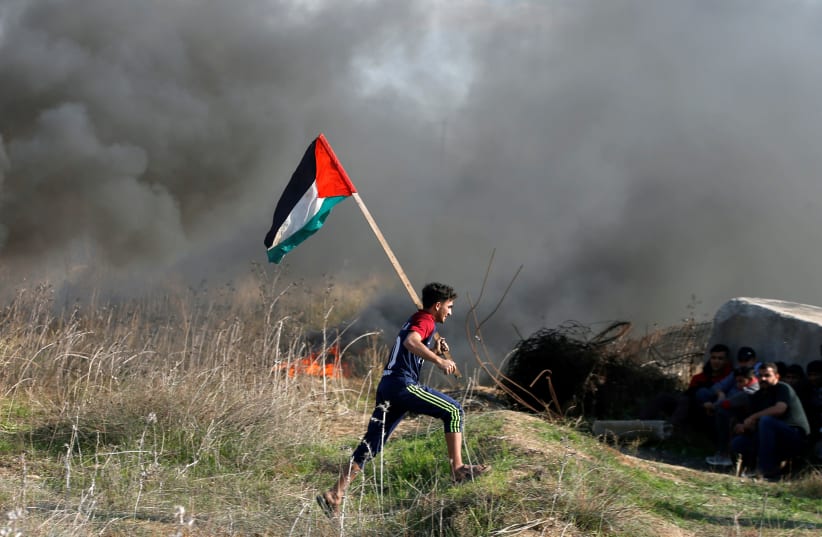 A protester holds a Palestinian flag as he runs during clashes with Israeli troops as Palestinians call for a "day of rage" in response to US President Donald Trump's recognition of Jerusalem as Israel's capital (photo credit: MOHAMMED SALEM/REUTERS)