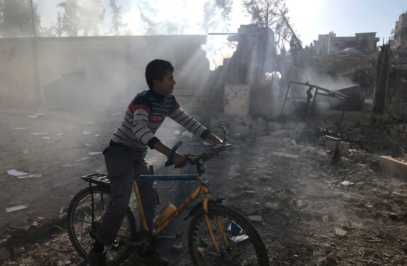 A Palestinian boy rides a bicycle near a militant target that was hit in an Israeli airstrike in the northern Gaza Strip (photo credit: MOHAMMED SALEM/REUTERS)