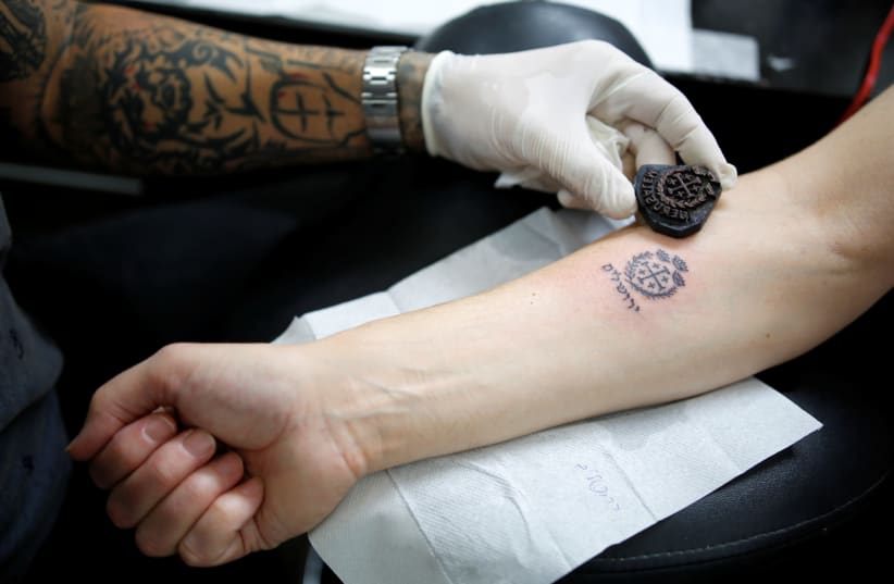Tattoo artist Wassim Razzouk holds an ancient wooden tattoo stamp near a tattoo he recently completed on his customer's arm at his studio in Jerusalem's Old City  (photo credit: AMIR COHEN/REUTERS)