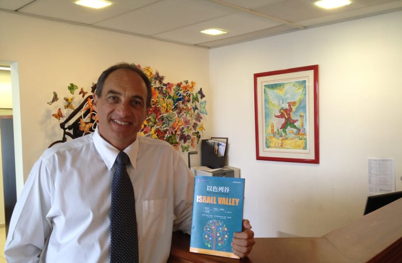 Israeli private equity investor Edouard Cukierman holds up a book he co-authored that was translated into Mandarin in 2014. Cukierman is focusing evermore on Chinese investment into Israel (photo credit: Courtesy)