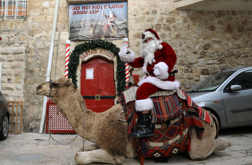  Issa Kassissieh, wearing a Santa Claus costume, rides a camel during the annual Christmas tree distribution by the Jerusalem municipality in Jerusalem's Old City December 21, 2017 (photo credit: AMMAR AWAD/REUTERS)