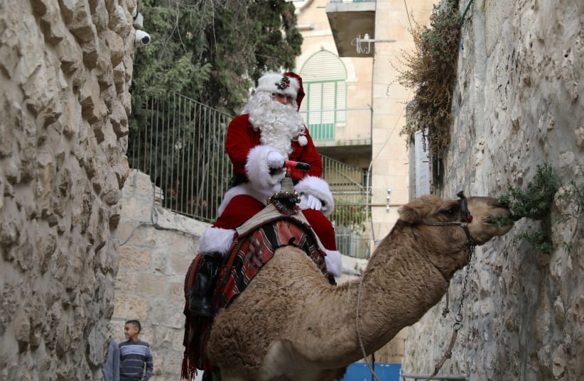  Issa Kassissieh, wearing a Santa Claus costume, rides a camel and distributes Christmas trees in Jerusalem's Old City December 21, 2017 (photo credit: AMMAR AWAD/REUTERS)