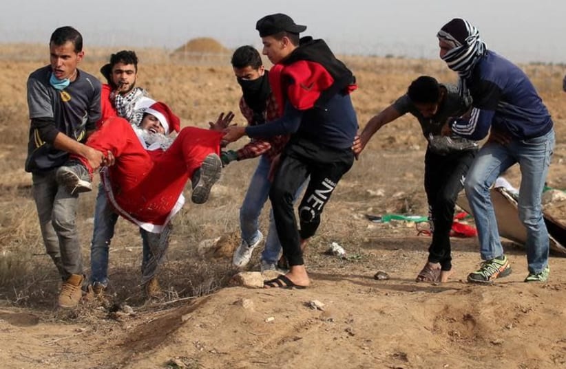  A wounded Palestinian demonstrator dressed as Santa Claus is evacuated during clashes with Israeli troops, at a protest as Palestinians call for a "Day of Rage" in response to US President Donald Trump's recognition of Jerusalem as Israel's capital, near the border with Israel in the southern Gaza  (photo credit: REUTERS/IBRAHEEM ABU MUSTAFA)