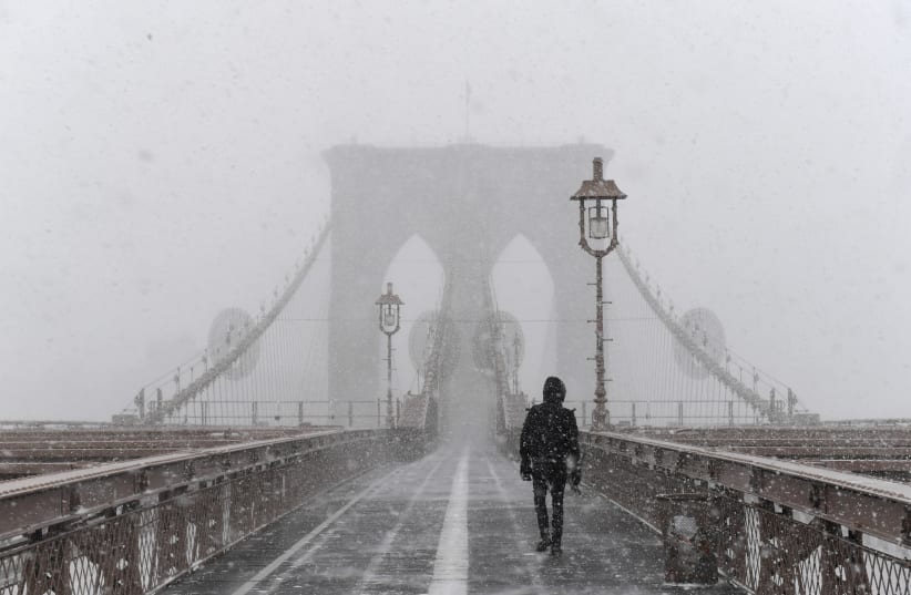 A pedestrian walks through blinding snow across the Brooklyn Bridge during Storm Grayson in New York City, U.S., January 4, 2018. (photo credit: REUTERS)