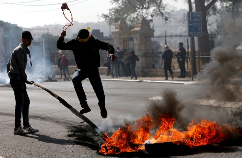A Palestinian demonstrator jumps over a burning tire in a protest in Bethlehem, January 2018 (photo credit: MUSSA QAWASMA / REUTERS)