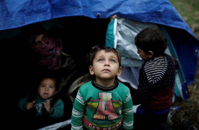 A Syrian refugee boy stands in front of his family tent at a makeshift camp for refugees and migrants next to the Moria camp on the island of Lesbos, Greece (REUTERS/Alkis Konstantinidis (photo credit: ALKIS KONSTANTINIDIS / REUTERS)