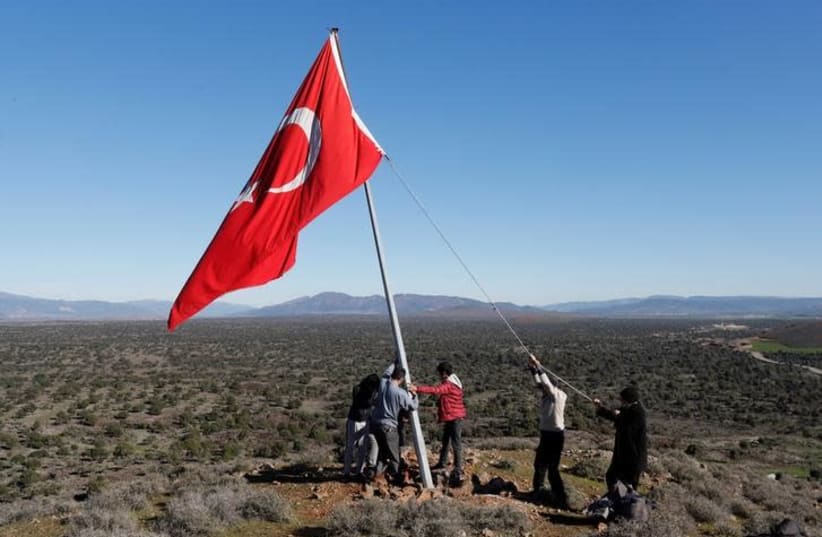 Villagers fix a broken flagpole in Sugedigi village on the Turkish-Syrian border in Hatay province, Turkey January 20, 2018 (photo credit: REUTERS/OSMAN ORSAL)