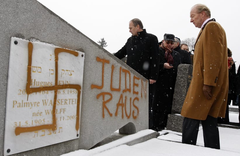 France's Interior Minister Brice Hortefeux walks next to a tombstone desecrated by vandals with a Nazi swastika and the Slogan "Jews Out", in the Jewish Cemetery of Cronenbourg near Strasbourg (photo credit: VINCENT KESSLER/ REUTERS)