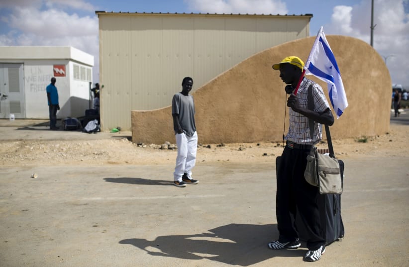 An African migrant holds an Israeli flag after being released from Holot detention centre in Israel's southern Negev desert August 25, 2015. (photo credit: REUTERS/AMIR COHEN)