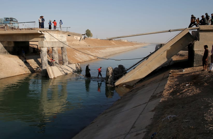 People cross a makeshift ladder in a village near Raqqa after a bridge was destroyed in fighting between the US-led coalition and Islamic State, in Raqqa, Syria, June 16, 2017 (photo credit: GORAN TOMASEVIC/REUTERS)