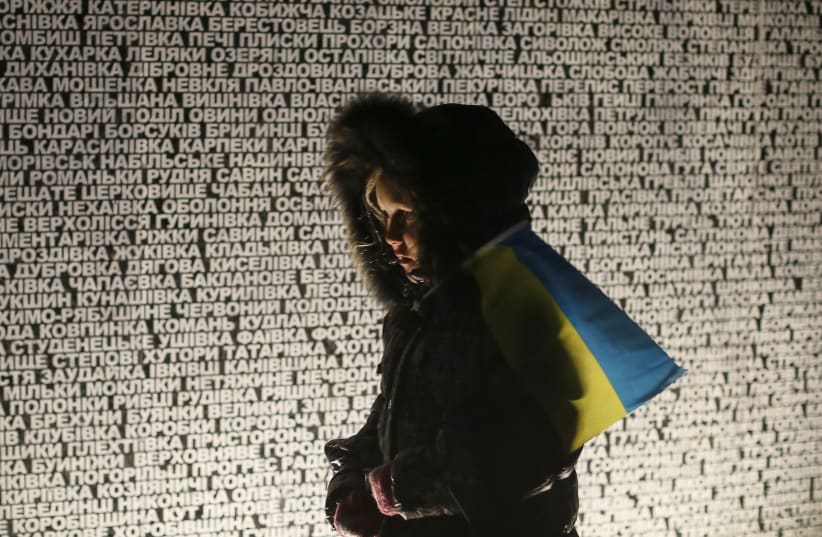 A girl holding a Ukrainian flag walks by a memorial commemorating the Holodomor (photo credit: GLEB GARANICH / REUTERS)