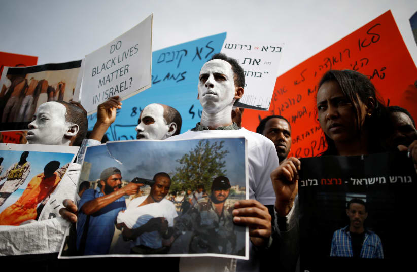 African migrants painted in white hold signs during a protest against the Israeli government's plan to deport part of their community, in front of the Rwandan embassy in Herzliya, Israel (photo credit: AMIR COHEN/REUTERS)