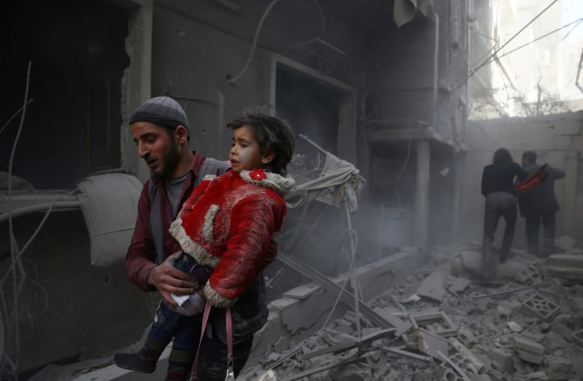 A man holds a child after an airstrike in the besieged town of Douma, Eastern Ghouta, Damascus, Syria February 7, 2018. (photo credit: REUTERS/BASSAM KHABIEH)