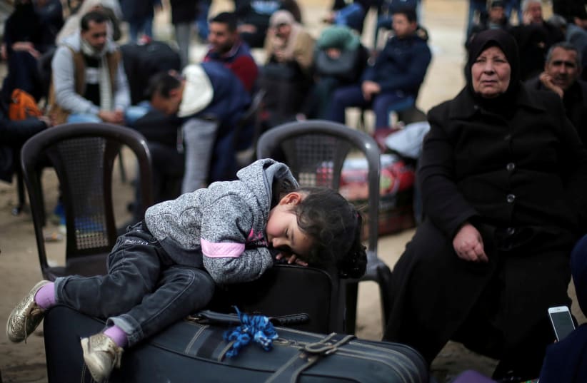 A girl sleeps on a suitcase as she waits with her family for a travel permit to cross into Egypt through the Rafah border crossing (photo credit: IBRAHEEM ABU MUSTAFA / REUTERS)