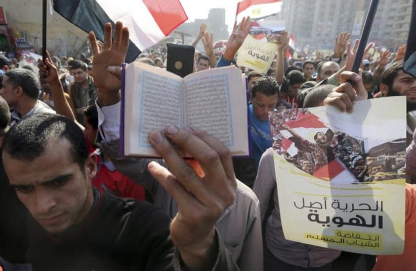 A supporter of the Muslim Brotherhood and ousted Egyptian President Mohamed Mursi holds a copy of the Koran as others shout slogans against the military and the interior ministry during a protest in the Cairo suburb of Matariya November 28, 2014. (photo credit: MOHAMED ABD EL GHANY/REUTERS)