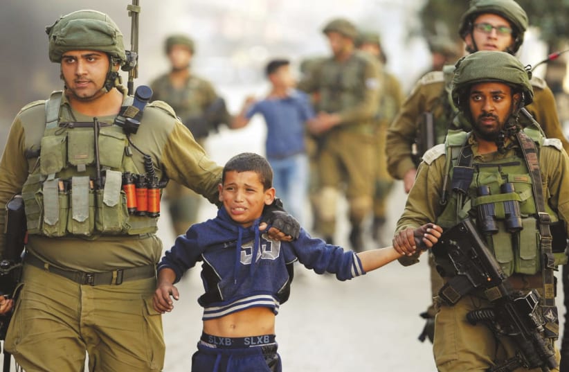 Soldiers detain a Palestinian boy during clashes in Hebron (photo credit: MUSSA QAWASMA / REUTERS)