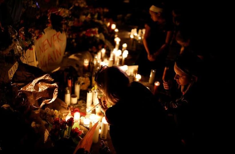 People light candles in front of mementoes placed in front of the fence of the Marjory Stoneman Douglas High School to commemorate the victims of the mass shooting, in Parkland, Florida, U.S., February 21, 2018. REUTERS/Carlos Garcia Rawlins (photo credit: CARLOS GARCIA RAWLINS/ REUTERS)