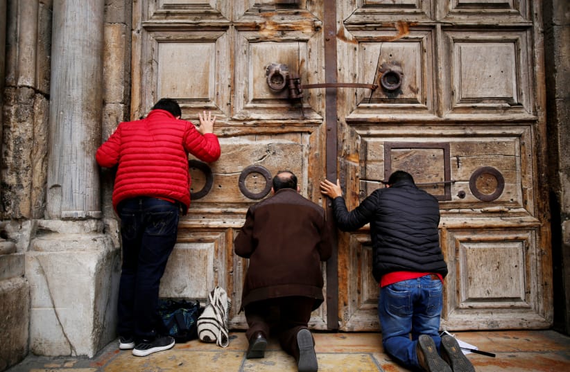 Worshippers kneel and pray in front of the closed doors of the Church of the Holy Sepulchre in Jerusalem's Old City (photo credit: AMIR COHEN/REUTERS)