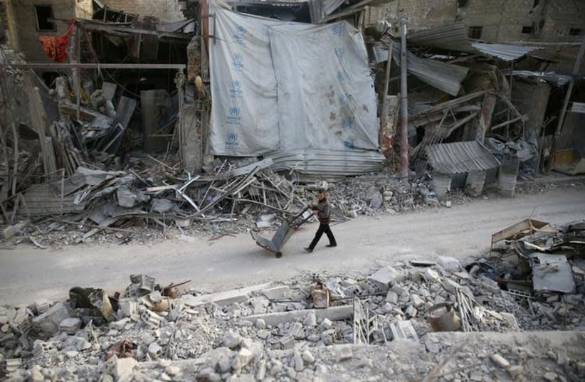 A man pushes a cart past damaged buildings at the besieged town of Douma, Eastern Ghouta, Damascus, Syria March 5, 2018. REUTERS/Bassam Khabieh (photo credit: REUTERS/BASSAM KHABIEH)