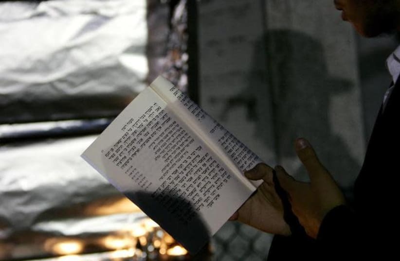 A man reads a prayer book outside (photo credit: SHANNON STAPLETON / REUTERS)