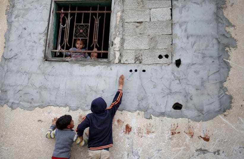 Palestinian children play as a girl held by her mother looks out of the window of house in the northern Gaza Strip February 12, 2018. Picture taken February 12, 2018 (photo credit: MOHAMMED SALEM/REUTERS)