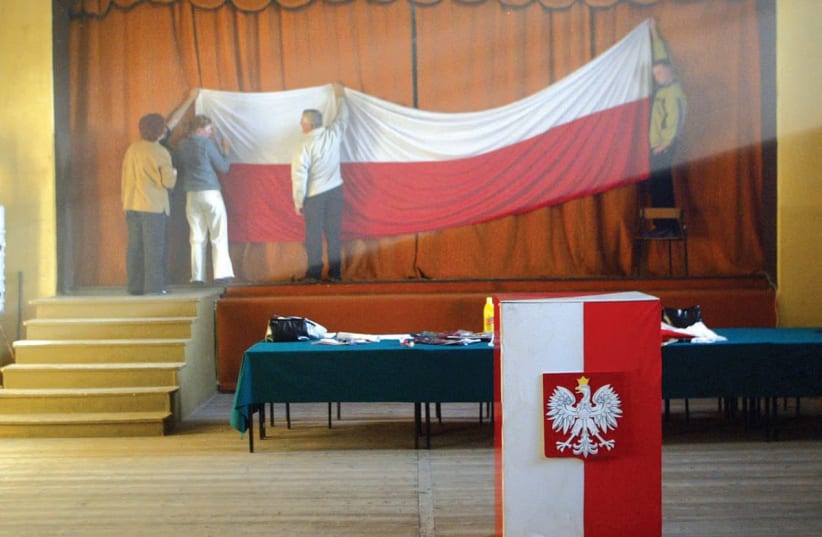MEN PUT up a Polish flag at an election booth. The country is struggling with its past. (photo credit: REUTERS)