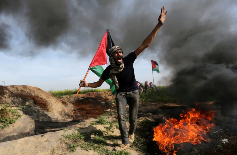A demonstrator holds a Palestinian flag as he shouts during clashes with Israeli troops, near the border with Israel in the southern Gaza Strip March 2, 2018. (photo credit: IBRAHEEM ABU MUSTAFA / REUTERS)