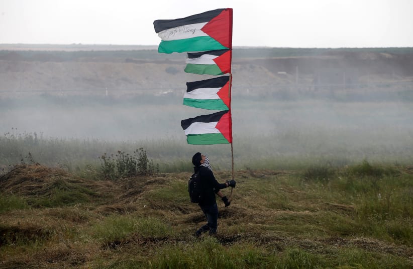 A demonstrator holds Palestinian holds during clashes with Israeli troops, during a tent city protest along the Israel border with Gaza, demanding the right to return to their homeland, east of Gaza City March 30, 2018. (photo credit: MOHAMMED SALEM/ REUTERS)
