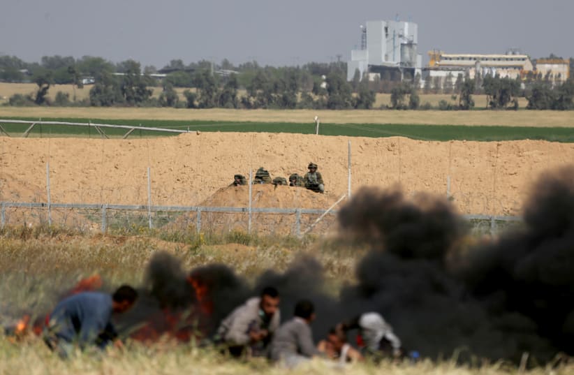 Palestinians take cover from Israeli snipers during clashes at the Gaza-Israel border at a protest in the southern Gaza Strip March 31, 2018 (photo credit: IBRAHEEM ABU MUSTAFA/REUTERS)