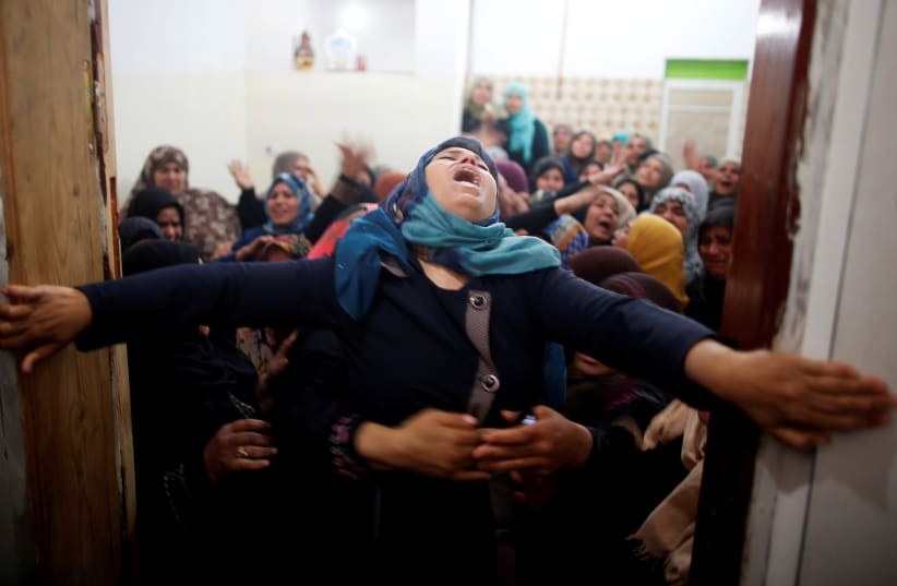 Mourners hold back a relative of Palestinian Hamdan Abu Amshah, who was killed along Israel border with Gaza (photo credit: REUTERS/SUHAIB SALEM)