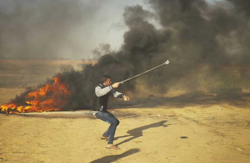 A Palestinian throws a rock towards Israeli forces on the Gaza border (photo credit: REUTERS)